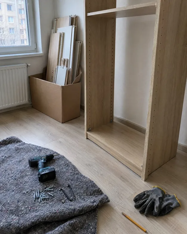 Rozpracovaná montáž skříně s aku vrtačkou a šroubky na dece